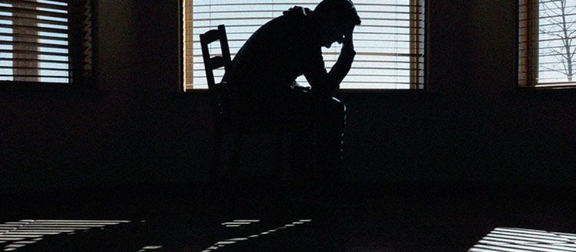 A man holds his head in his hands as he sits on a bed