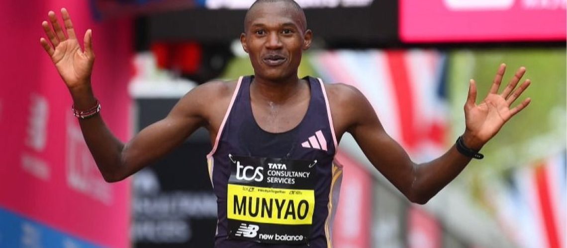 Alex Mutiso, wearing black running gear, raises his arms in the air after winning a long-distance race.