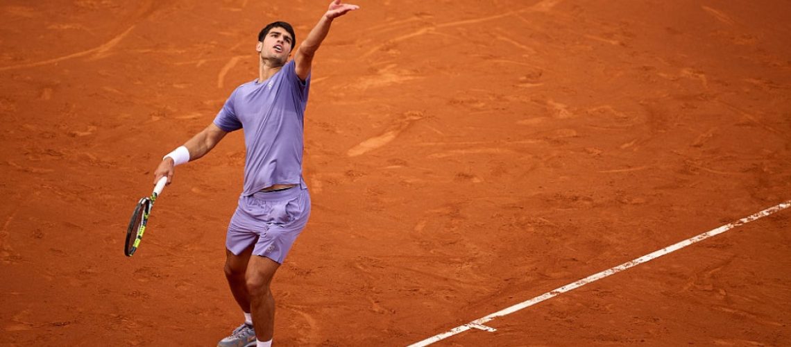 Carlos Alcaraz, dressed in lilac, serving on a clay court at Real Club De Tenis Barcelona