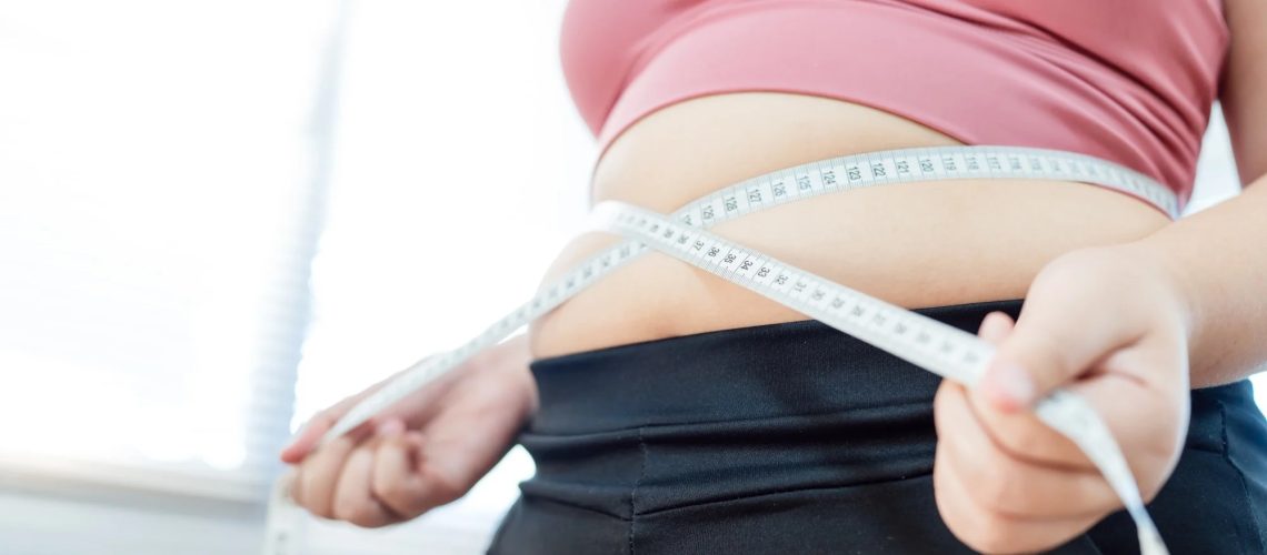Overweight woman in pink sports top pulling measuring tape around waist