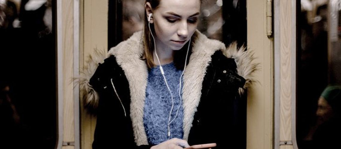 A woman standing in a subway car listens to music on her iPhone