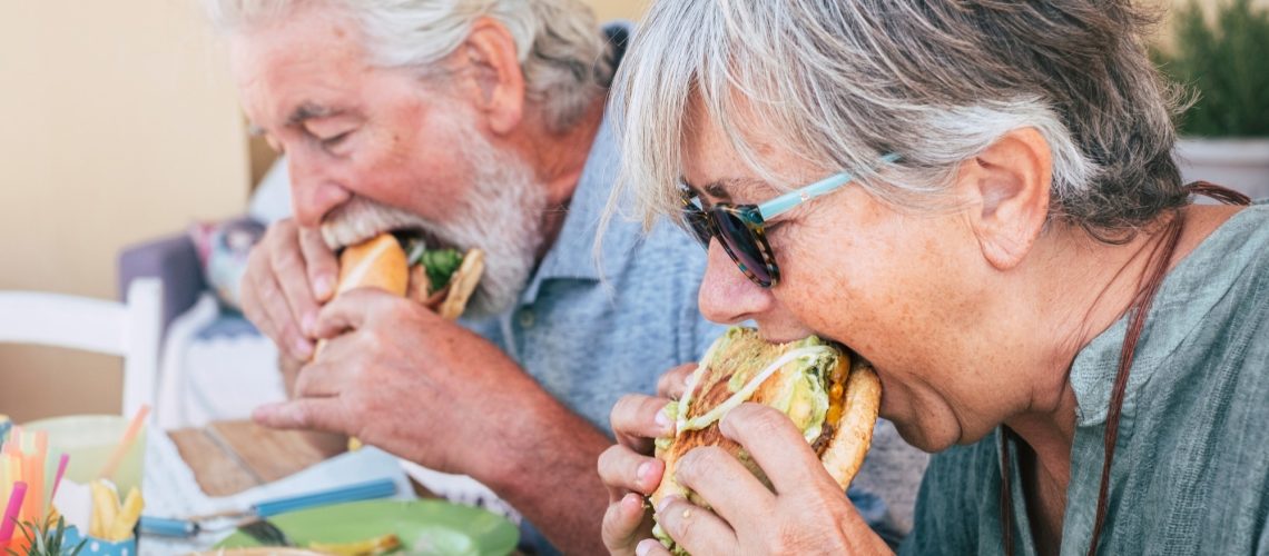 Couple of senior man and woman eating burgers