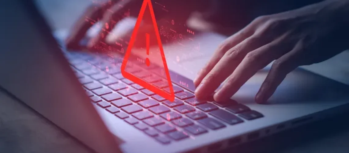 Hands on a laptop with a warning exclamation point