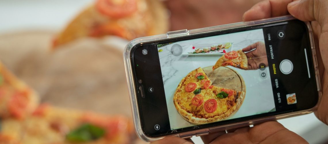 Person taking photo of pizza with smartphone