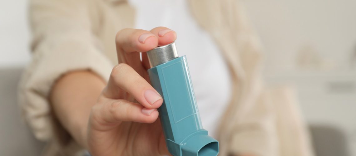 Woman holding asthma inhaler indoors, closeup