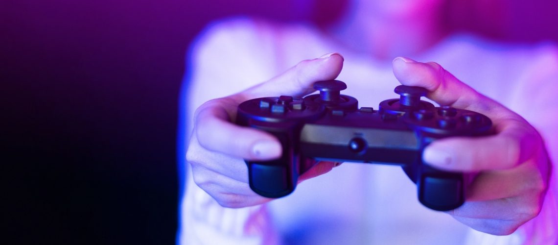 A woman is seen holding a video game controller in front of a vibrant purple light, engaged in a gaming session.