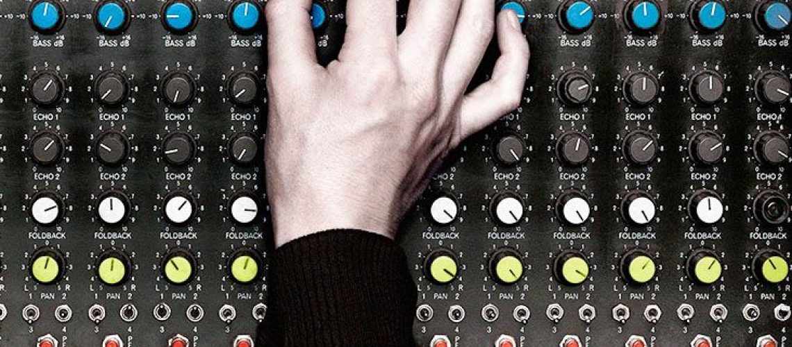 A hand turns up a knob on an audio board