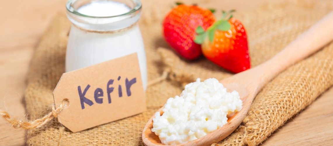 Kefir grains in wooden spoon in front of cups of Kefir Yogurt Parfaits.