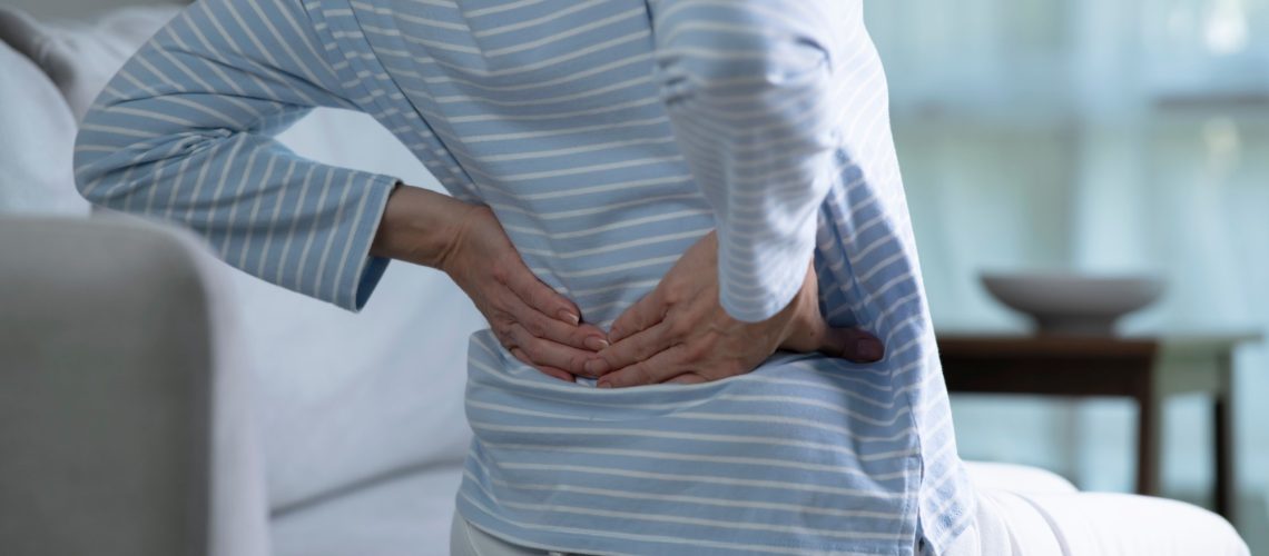 senior woman on sofa feeling and suffering from back pain and lower lumbar discomfort