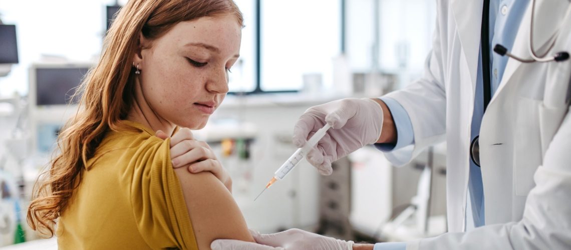pediatrician injecting vaccine into teenage girl arm
