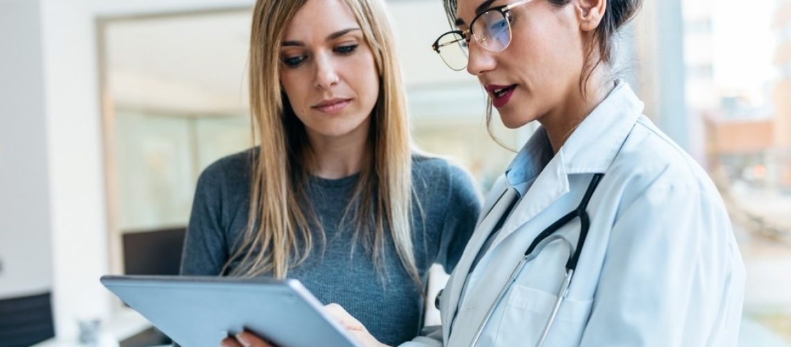 Female doctor talking while explaining medical treatment with digital tablet to patient in the consultation