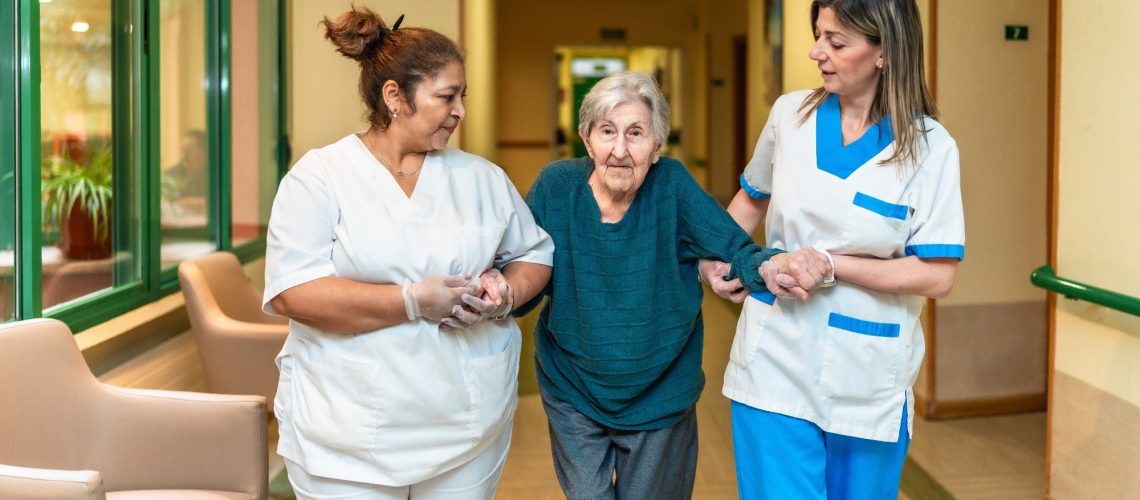 Two nurses assisting an elderly woman walking
