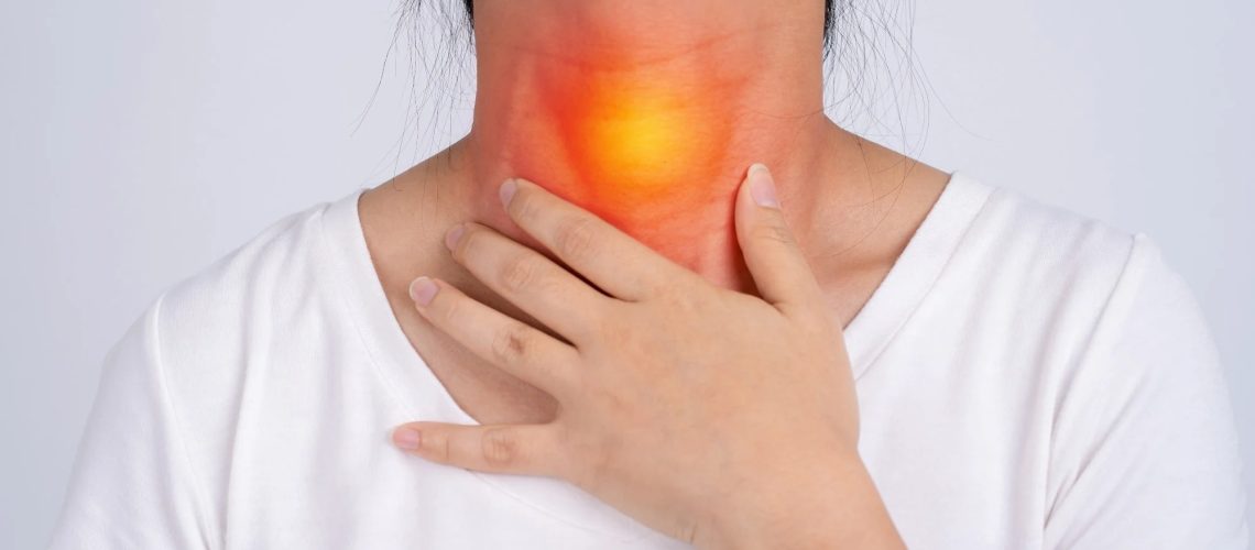 A woman holds her hand to the front of her neck, with a red and yellow glow highlighting the throat area to represent pain or discomfort.