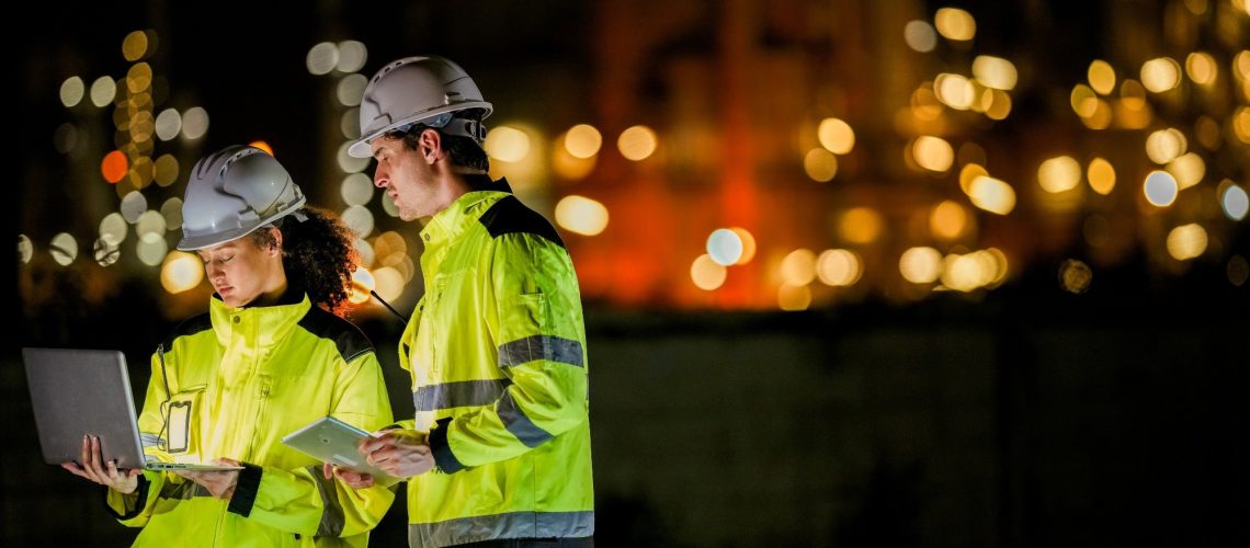 Two engineers collaborate on a night shift using a laptop and tablet
