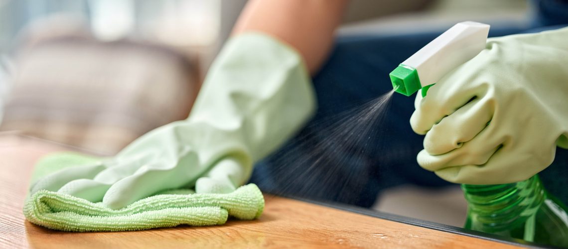 Spraying cleaner on wooden table with cloth