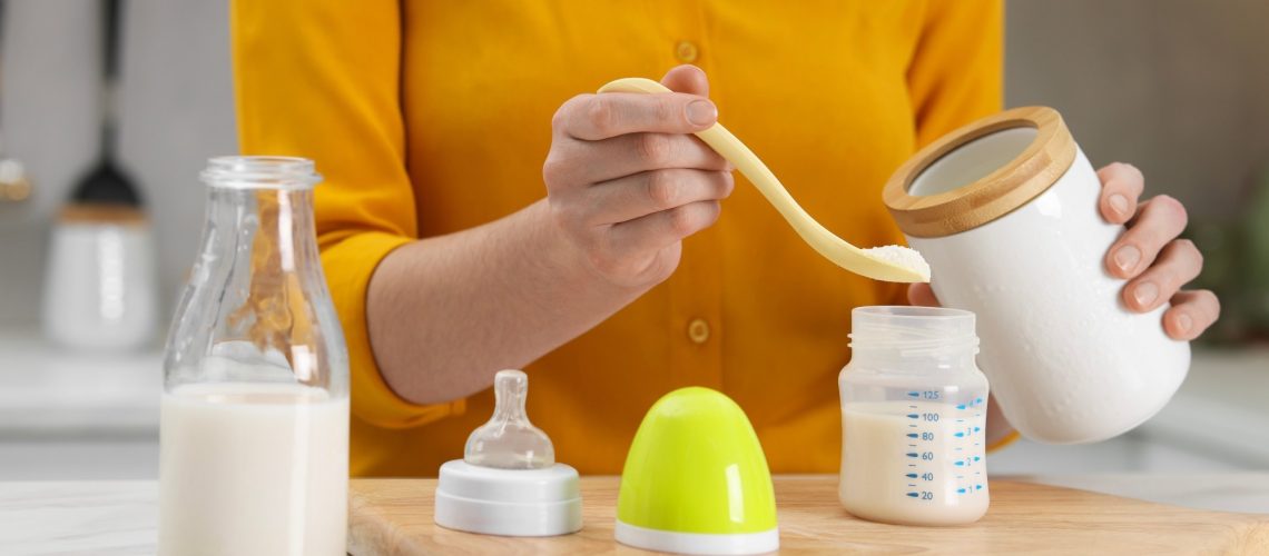 Mother making baby formula in feeding bottle at table