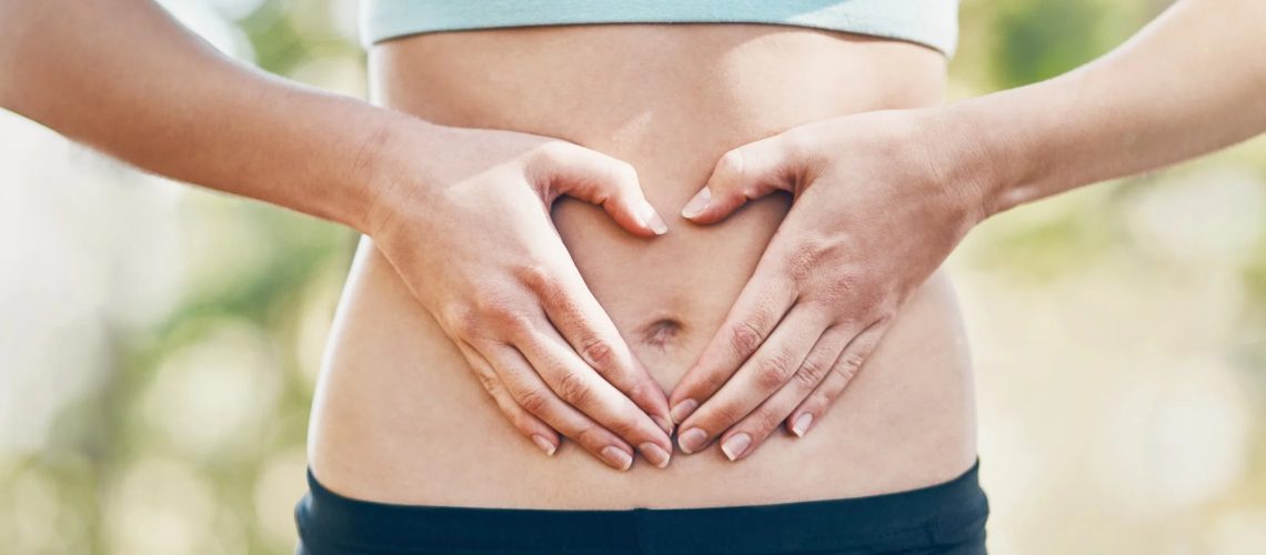 Abdomen of woman in sports gear. Hands are across stomach in the shape of a heart for gut health