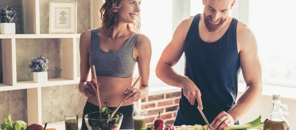 young sports people are talking and smiling while cooking healthy food in kitchen at home
