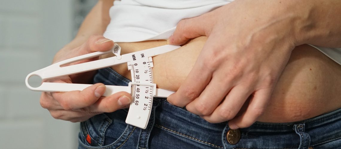 A woman in a white T-shirt and navy blue jeans measures the level of body fat with a special device