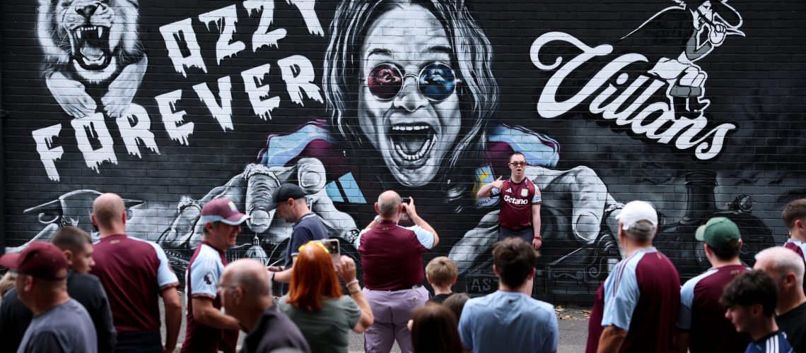 Fans pose for a photo in front of an Ozzy Osbourne mural prior to during the Premier League match between Aston Villa and Newcastle United at Villa Park on August 16, 2025 in Birmingham, England.