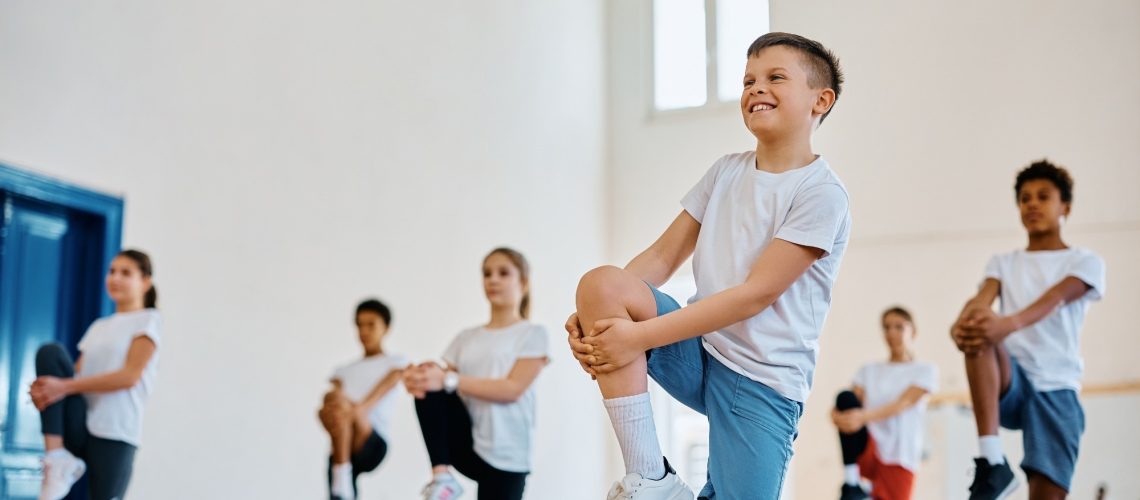 Happy student and his classmates practicing on PE class at school gym.