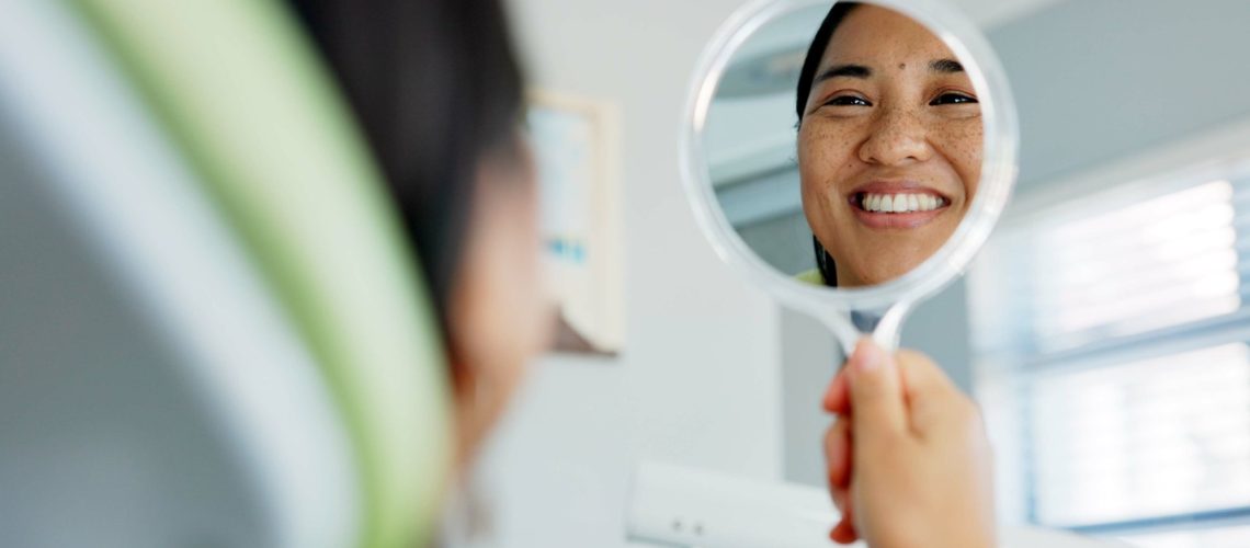 Happy woman with mirror check at a dentist for teeth whitening results