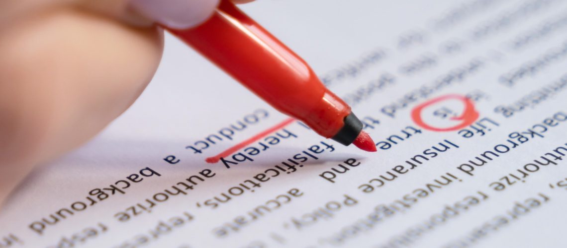 A person uses a red pen to mark and correct text on a printed document.