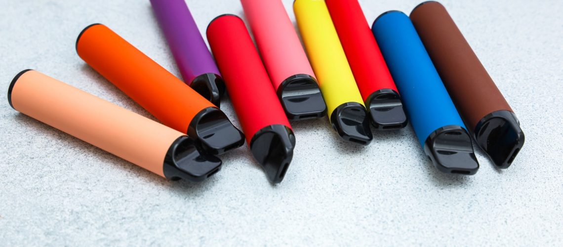 Collection of colorful vape pens arranged on a neutral gray surface.