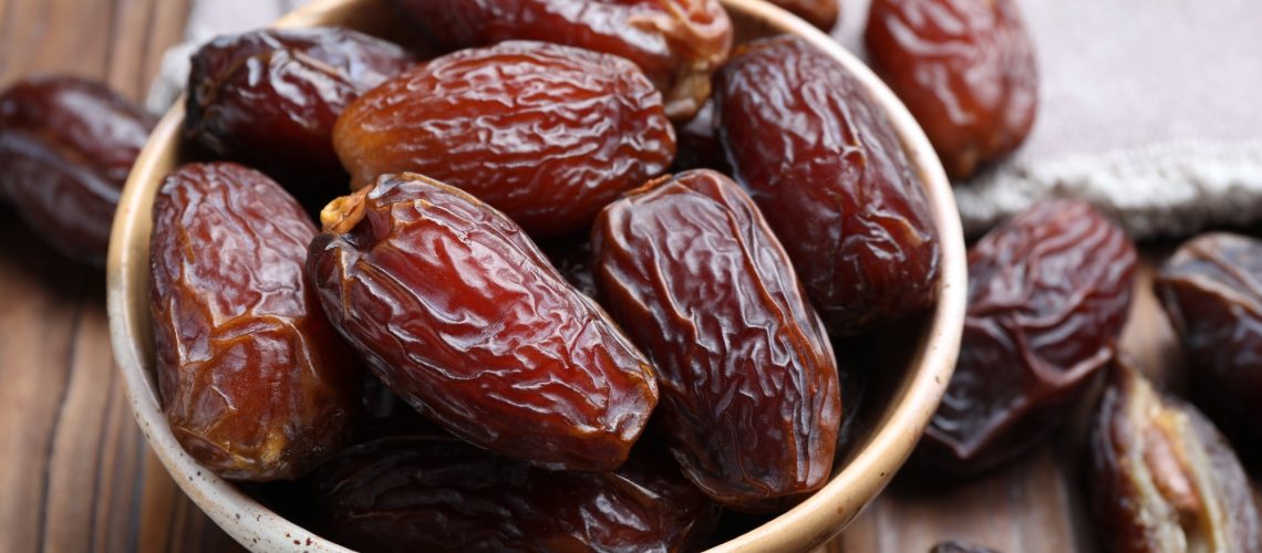 Many tasty dried dates in bowl on wooden table, closeup