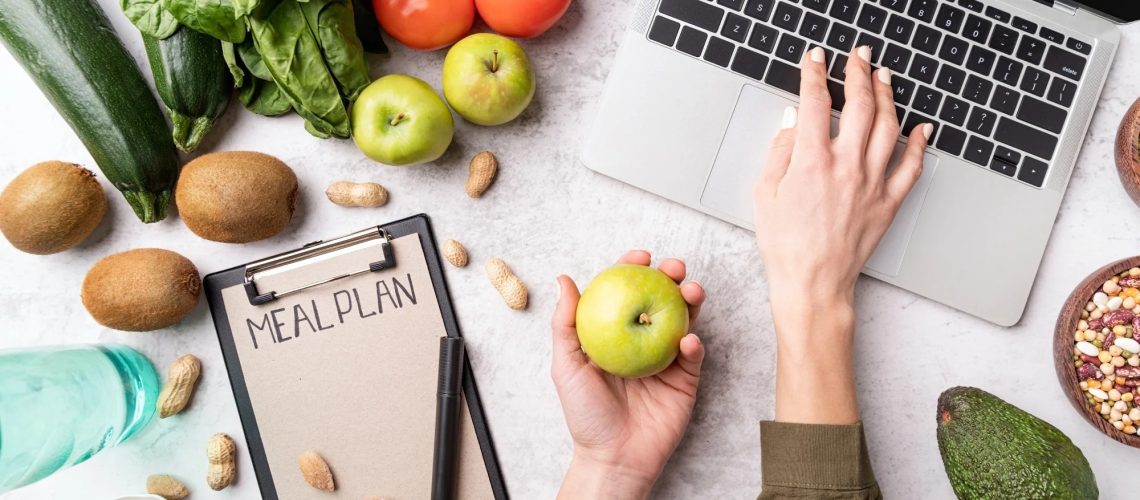 Woman workspace with healthy food. Female hands writing in the notepad words