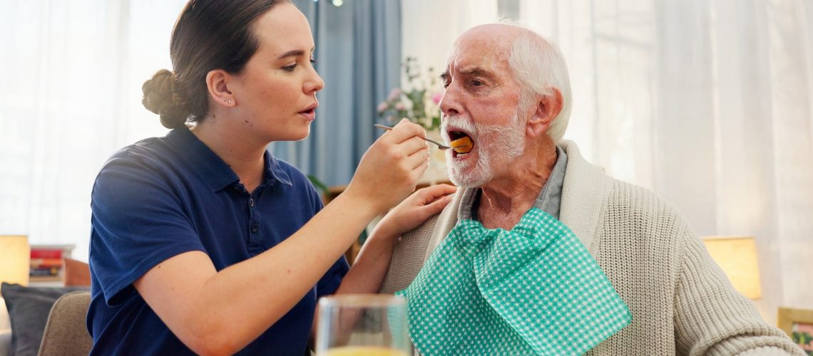 Female healthcare work feeding an elderly male patient with a spoon