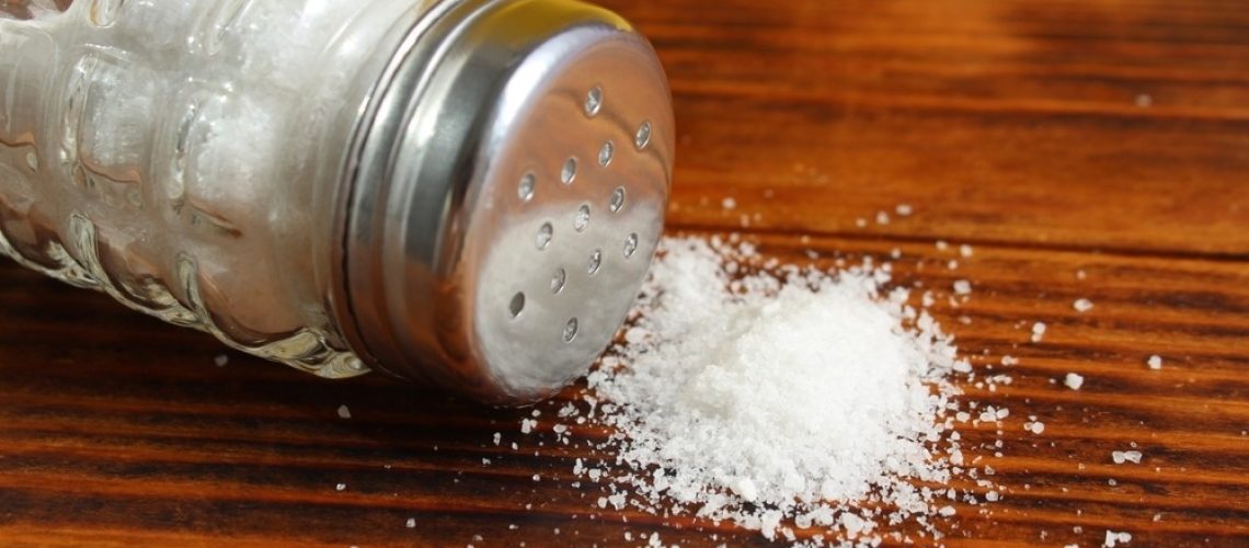 On a wooden table lies a glass salt shaker with overturned salt.