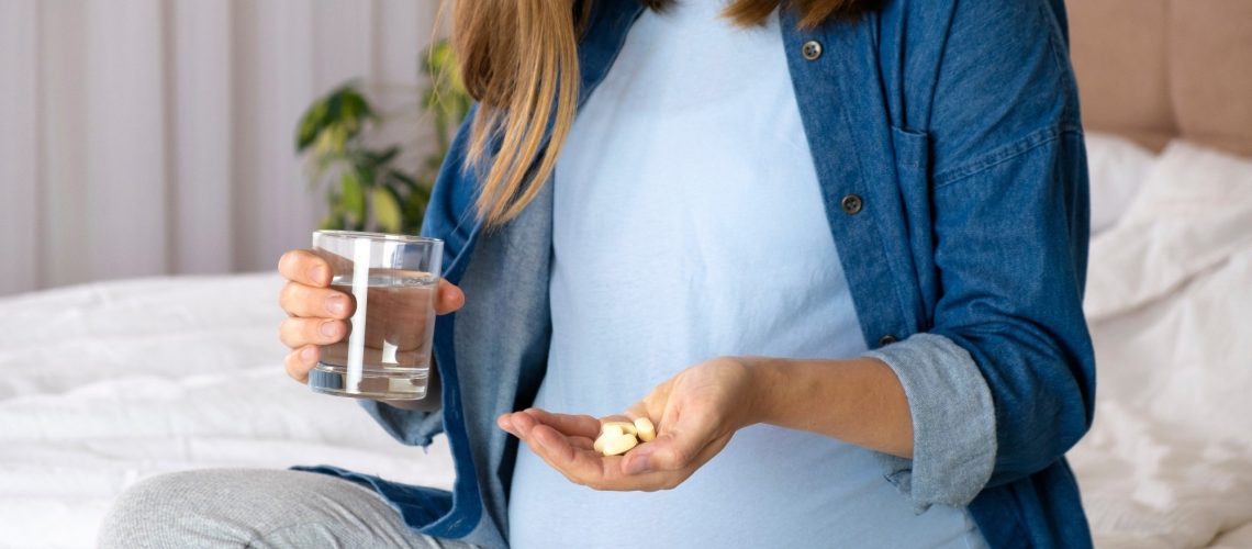Pregnant woman hold pills and glass of water.