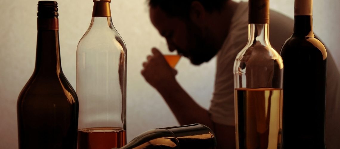 silhouette of anonymous alcoholic person drinking behind bottles of alcohol