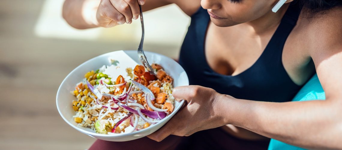 sporty young woman eating a bowl of vegan salad
