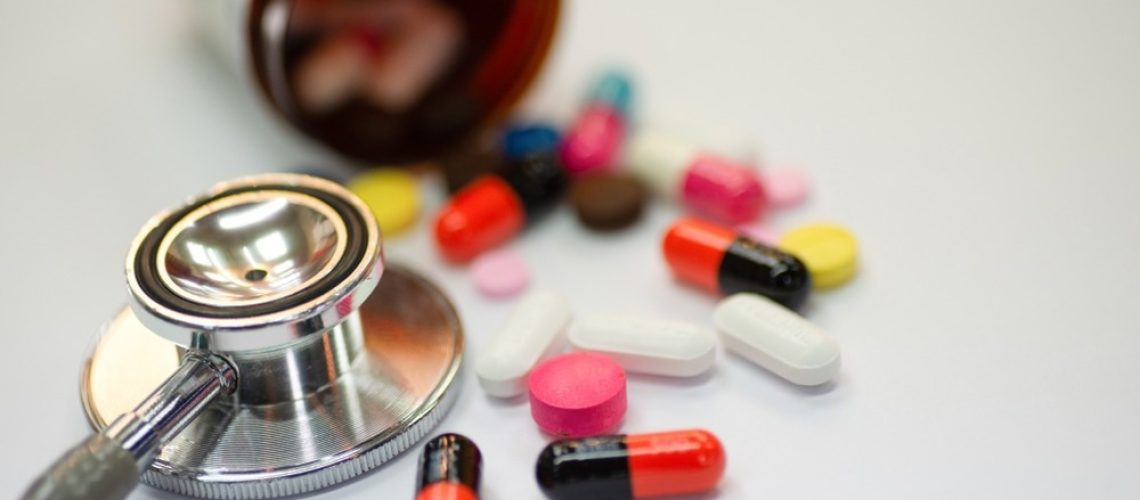Close up of statin and beta-blocker pills and capsules with bottle and stethoscope