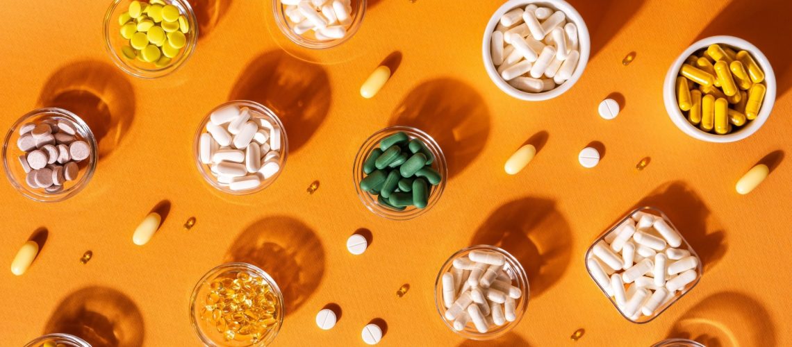 Organic dietary supplements, many capsules of vitamins and minerals in small bowls from above on an orange background.